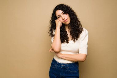 Sıkılmış genç bir kadın, stüdyonun arka planında kameraya bakarken yorgun ve sinirli görünüyor.