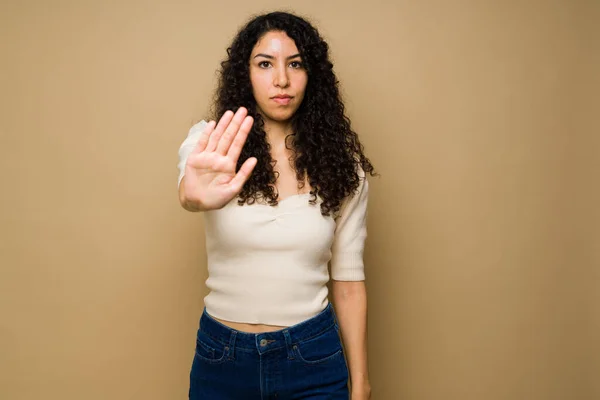 Upset mexican young woman showing her palm hand and doing a stop gesture looking angry