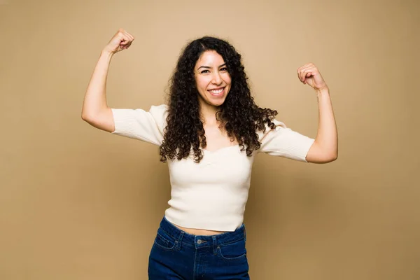 Strong mexican woman with curly hair showing her biceps and smiling while feeling powerful
