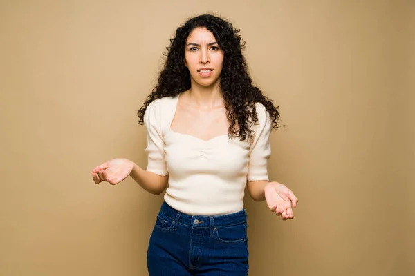 Frustrated hispanic woman shrugging her shoulders looking annoyed and with a lot of doubts