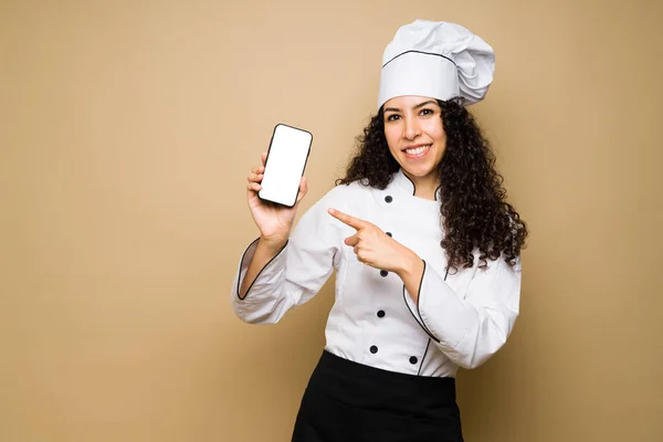 Attractive woman chef or cook smiling while pointing to her smartphone for a food delivery app or social media