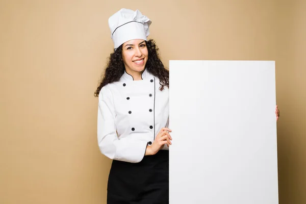 Happy woman chef or cook holding a blank banner showing the food menu or ad about a restaurant