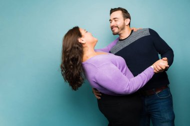 Romantic young couple in love dancing during a date while smiling against a blue studio background
