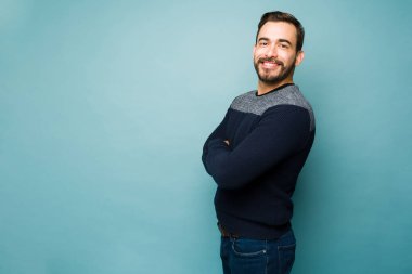 Happy handsome young man crossing his arms and smiling with casual clothes while standing on a studio background with copy space