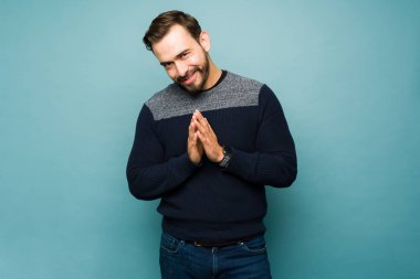 Mischievous caucasian young man making a plan and rubbing his hands together while looking happy making eye contact