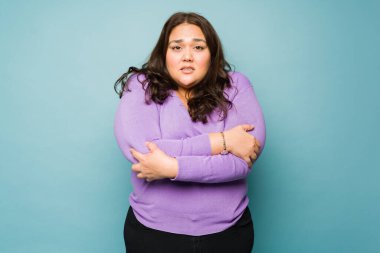 Upset latin overweight woman feeling cold and shivering looking sad against a studio background
