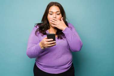 Surprised fat woman covering her mouth looking shocked while texting or looking at social media on the smartphone