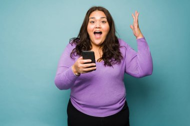 Portrait of a surprised happy young woman looking excited due to good news while texting on the smartphone