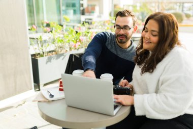 Beautiful happy influencer woman and man editing a social media video on the laptop while working at the coffee shop