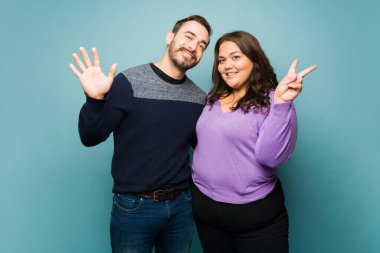Cheerful young couple waving hello and doing the peace sign to friends while making eye contact