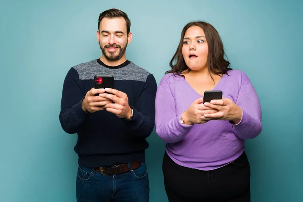 在用智能手机给另一个女人发短信的同时 惊慌失措的胖女人在偷窥他那欺骗的快乐男友 — 图库照片