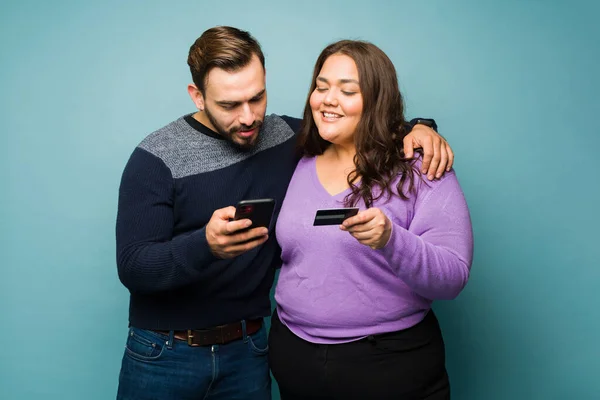 スマートフォンでオンラインショッピングをしながらクレジットカードで支払いながら抱きつく幸せな笑顔のカップル — ストック写真