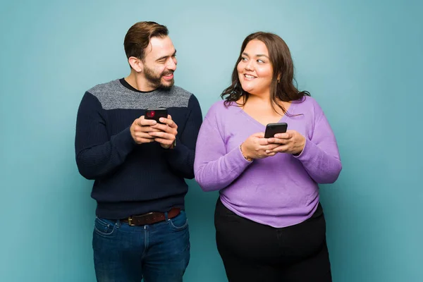一对快乐的年轻夫妇一边微笑着 一边用智能手机在蓝色工作室的背景下一起发短信 — 图库照片
