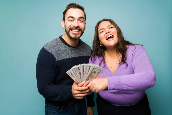 Super excited young couple showing a lot of money and feeling rich while celebrating in front of a studio background