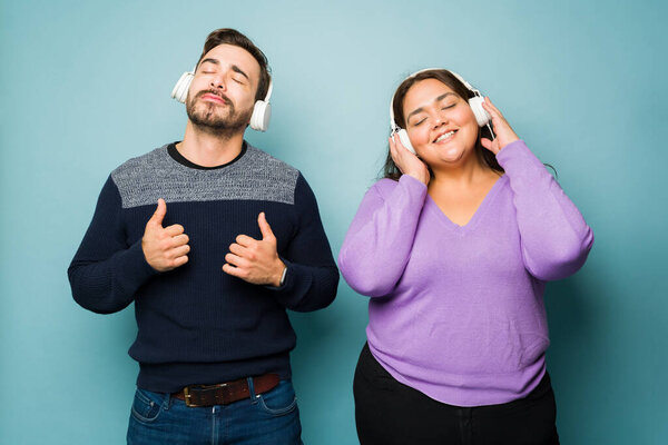 Relaxed caucasian boyfriend and obese hispanic girlfriend using headphones to listen to music together