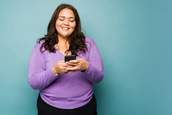 Cheerful beautiful big woman laughing and looking happy while texting or using social media on the smartphone