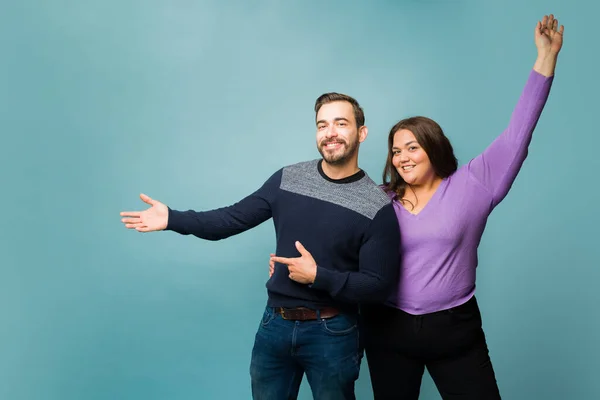 Cheerful young man and obese latin woman celebrating while showing an ad in copy space