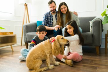 Cheerful little girl and boy petting and playing with their beautiful yellow cocker spaniel dog with the company of their parents at home