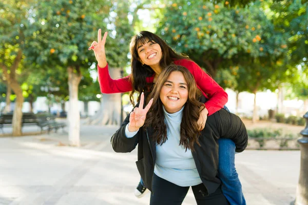 Smiling Women Best Friends Doing Piggy Back Peace Sign While — Stockfoto