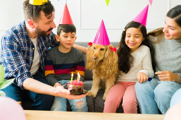 Cheerful family and children ready to blow the birthday candles and eat cake while celebrating their dog\'s birthday party at home