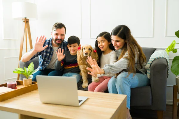 Excited parents and little children at home waving hello to family during a video call on the laptop