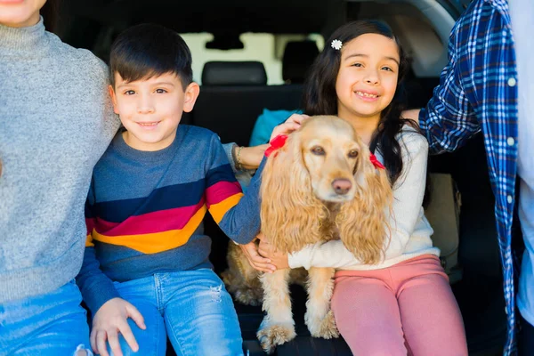 Cheerful little children smiling looking happy while sitting in the car trunk ready for a road trip with their beautiful dog and family