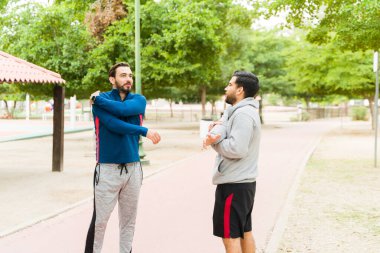 Fitness young men doing warm up exercises and stretching their arms while preparing to start running together at the park