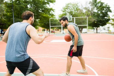 Fit young men friends at the park playing a one on one game of basketball while exercising