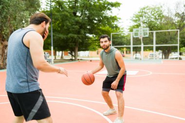 Fit young men playing a one on one game of basketball at the park court while exercising 
