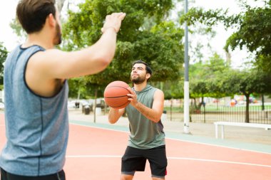 Fit young man ready to score and throw the ball in the hoop while playing basketball with a friend
