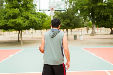 Latin active man seen from behind practicing and playing basketball alone on the court