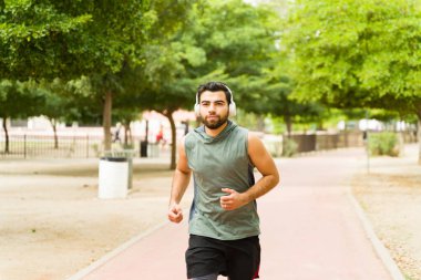 Fit young man running in the park wearing headphones listening to music while working out