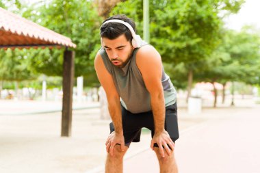 Tired runner catching his breath and resting after finishing running with headphones in the park