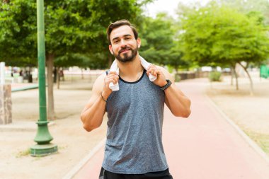 Attractive caucasian man smiling using a towel and smiling while working out outdoors in the park