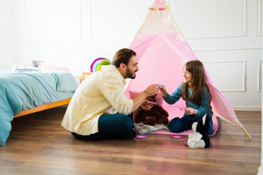 Happy father and young daughter smiling playing tea in the bedroom with a pink teepee and having fun