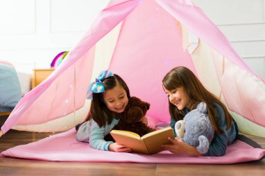 Adorable best friends kids smiling while reading a children's book and fairy tale while playing together