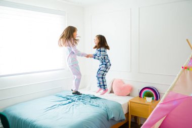 Cheerful kid laughing while jumping and playing in bed in pajamas during a fun sleepover