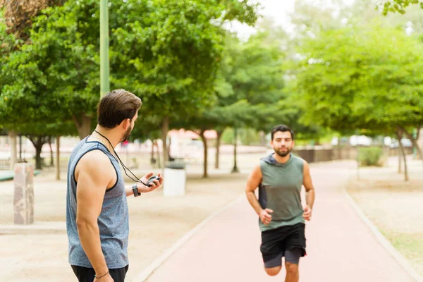Caucasian personal trainer using a timer while checking the time of an active runner exercising outdoors
