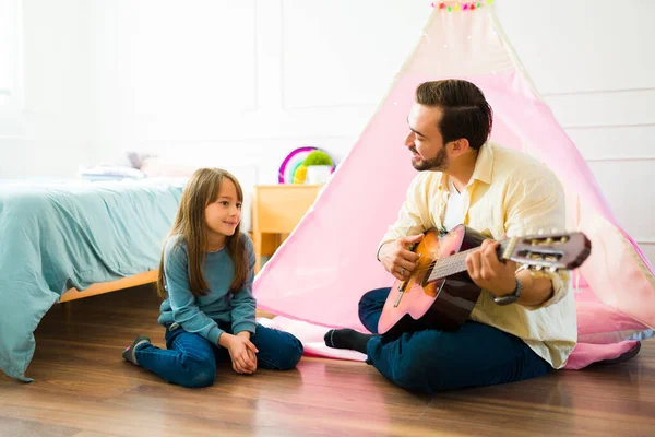 Happy father playing guitar and singing a song to her beautiful caucasian daughter while playing