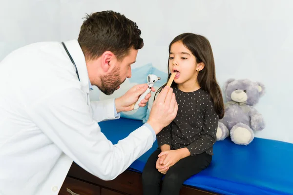 儿科医师在进行体格检查时 用耳镜检查一个可爱的小孩的喉咙和嘴 — 图库照片
