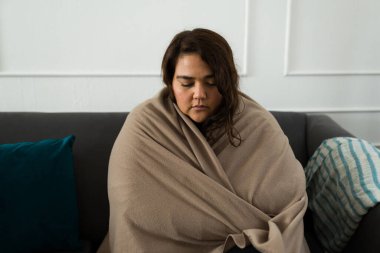 Lonely sad big woman wrapped in a blanket feeling sad and depressed at home after crying on the sofa