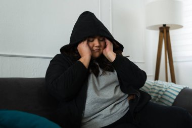 Stresli, aşırı kilolu, siyah kapüşonlu, depresif görünümlü, baş ağrısı ve depresyon çeken bir kadın. 
