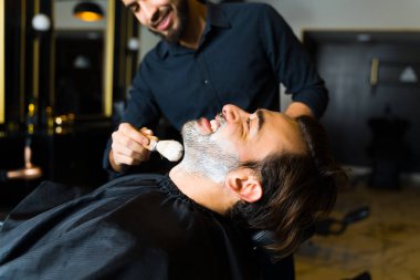Cheerful caucasian man smiling and laughing at the barber shop while having fun shaving his beard