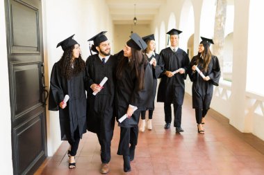 Cheerful group of friends hugging while walking after attending their graduation ceremony and getting their college diplomas