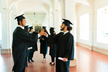 Latin mexican friends at university shaking hands and saying congratulations after their graduation ceremony 