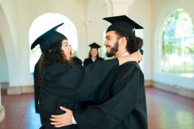 Happy couple hugging and looking at each other while celebrating getting their college diploma during graduation
