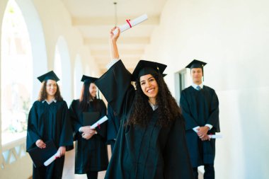 Excited young woman feeling proud showing her college diploma and celebrating with friends during graduation ceremony