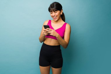 Gorgeous fit young woman laughing while texting on the smartphone before her workout exercises