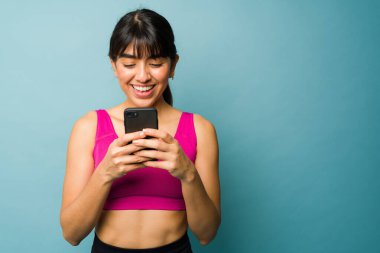 Beautiful woman texting on the smartphone and using a fitness app for her workouts next to copy space in front of a blue background