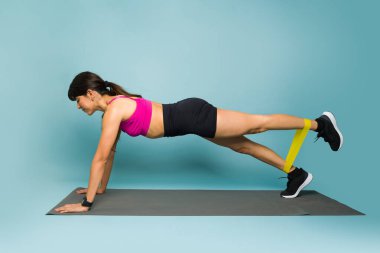 Side view of an athletic young woman doing plank exercises using a resistance band and exercise mat during her workout